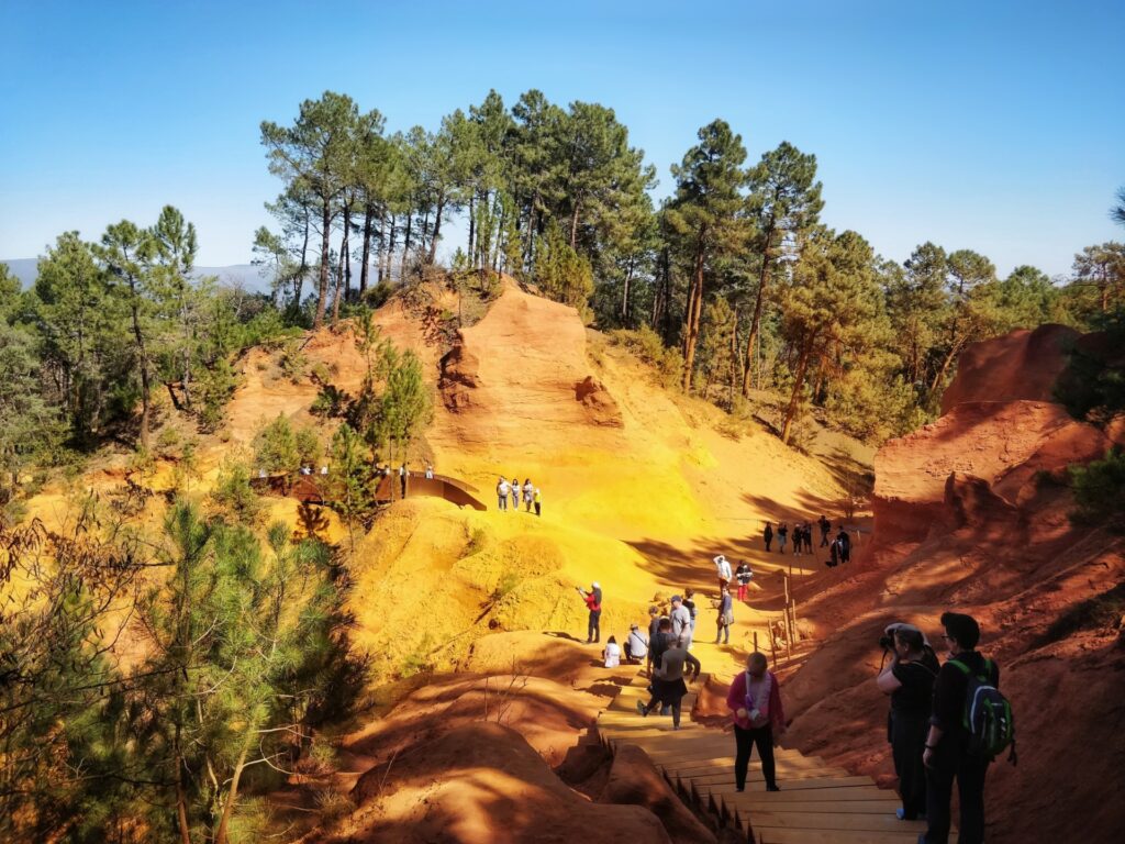 Roussillon Provence ochre-color rocks, trees on top of hill, people on path