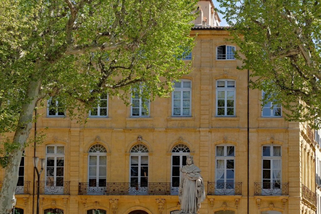 yellow brick building in Aix-en-Provence with a fountain of king Rene and green trees