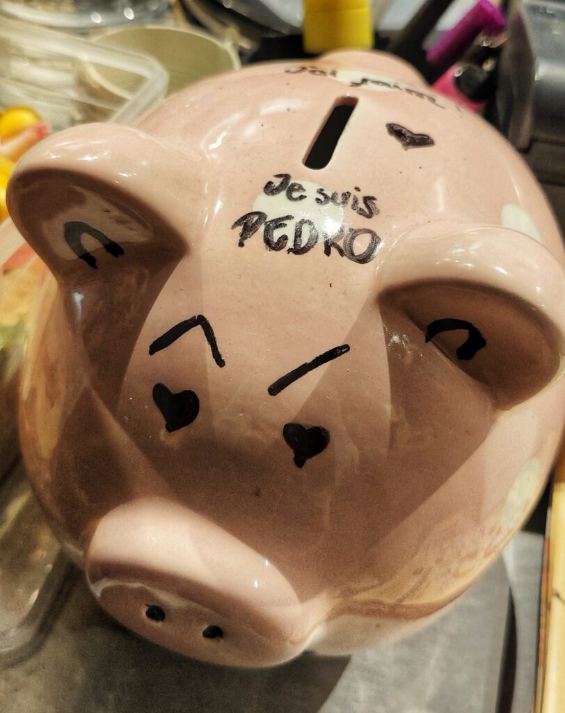 Pink piggy bank with the words "Je suis Pedro" meaning "I am Pedro" written in black marker on top.