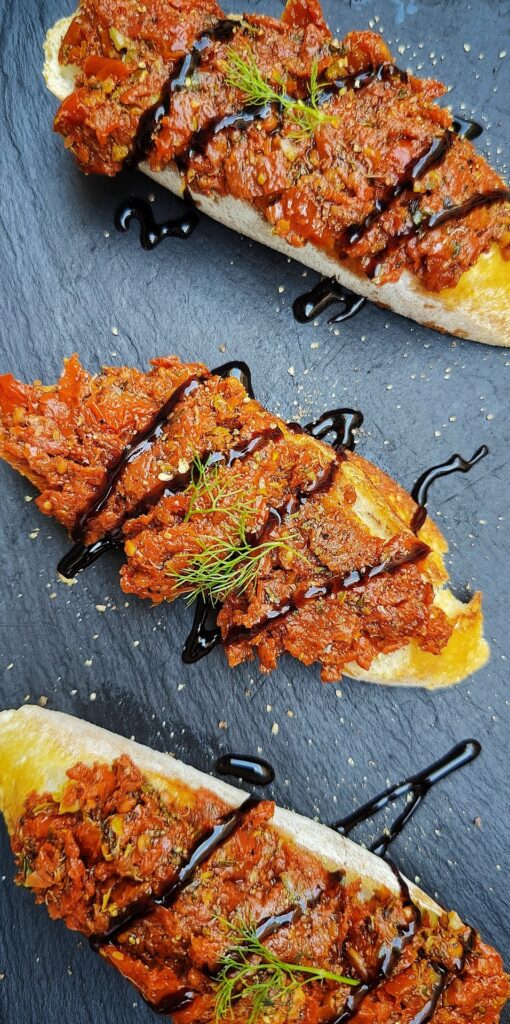 Three bruschettas drizzled with balsamic vinegar on a stone slab as seen from above