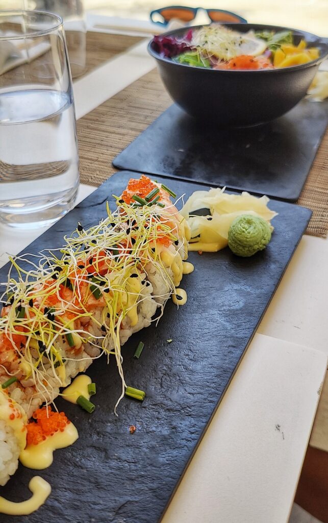 Sushi roll on a black rock slab plate and a poke bowl in the background