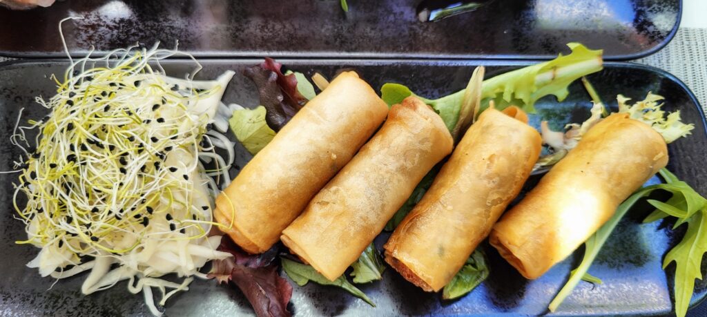 four spring rolls with fresh sprouts on a black plate