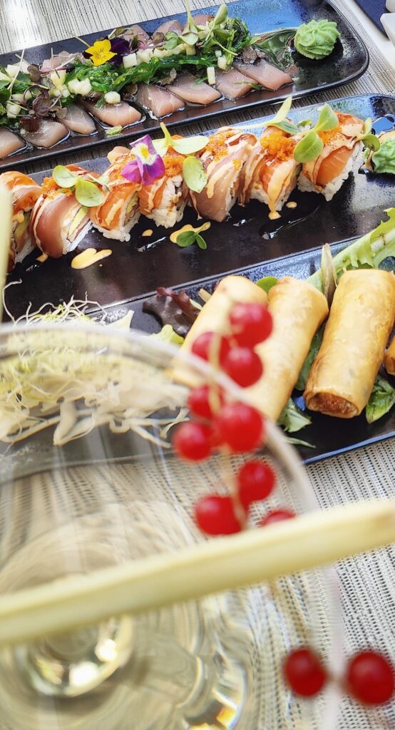 Cocktail garnished with red currant and sushi rolls with Japanese spring rolls 