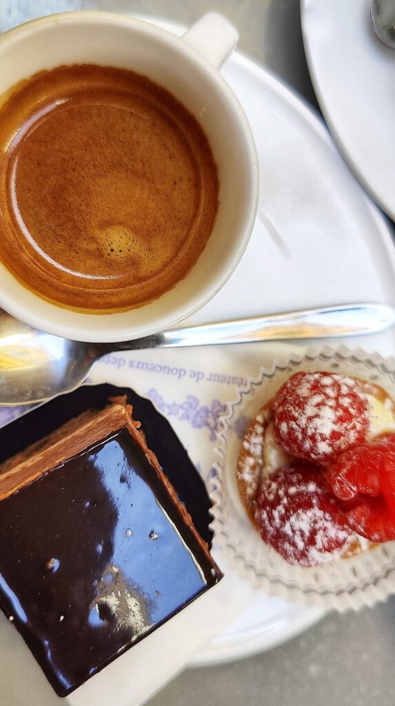 A cup of espresso with two desserts: a chocolate cake and a raspberry tart as seen from above.