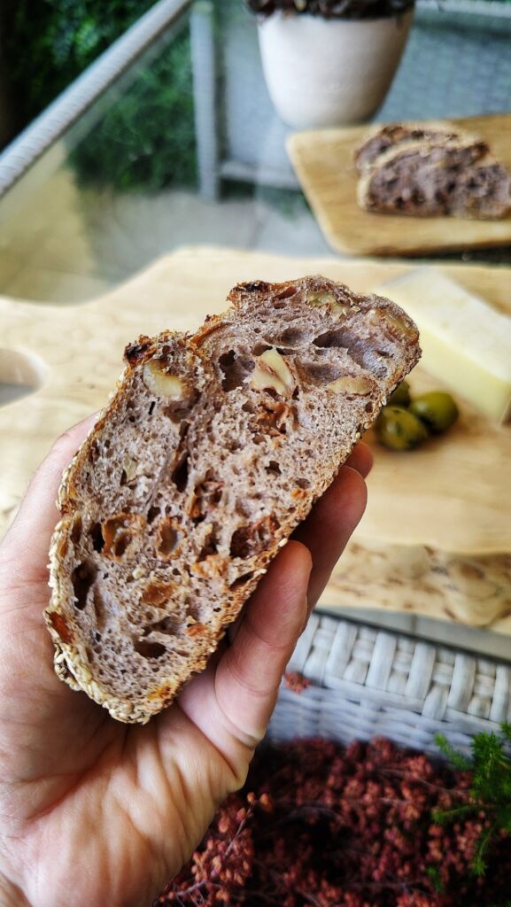 Hand holding a nut and raisin slice of bread. Wooden cutting board in the background.